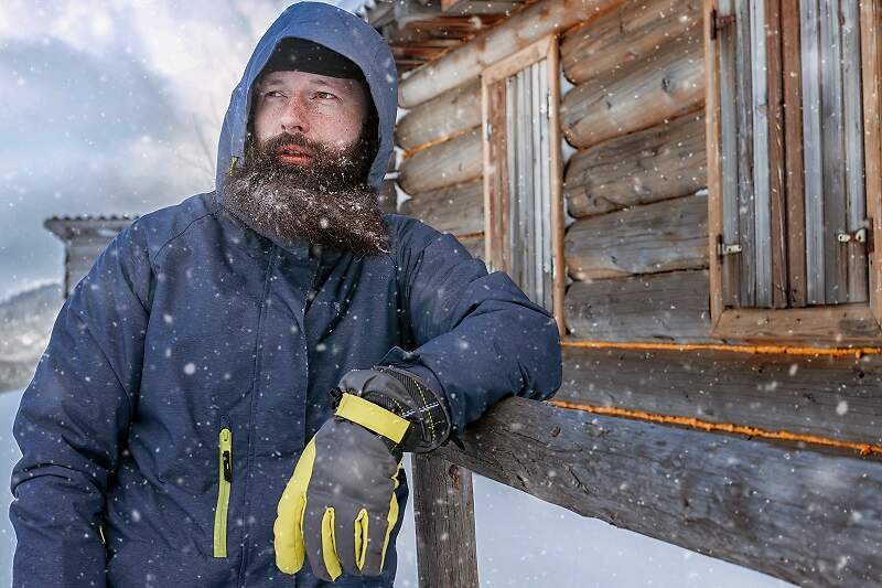 Bearded man in winter, adventure mountain man with a beard in the snow. Background of the old village